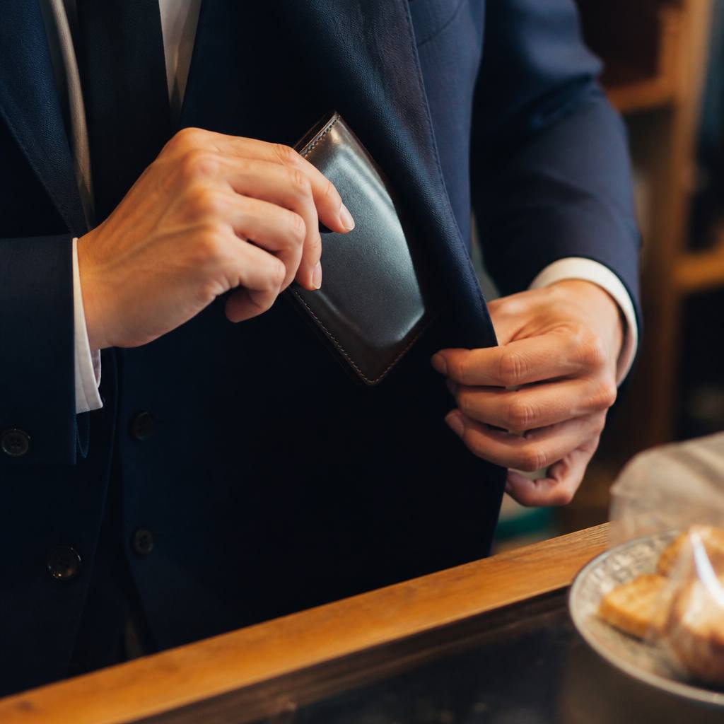 カフェの会計でジャケットの男性がコードバン財布を取り出す手元